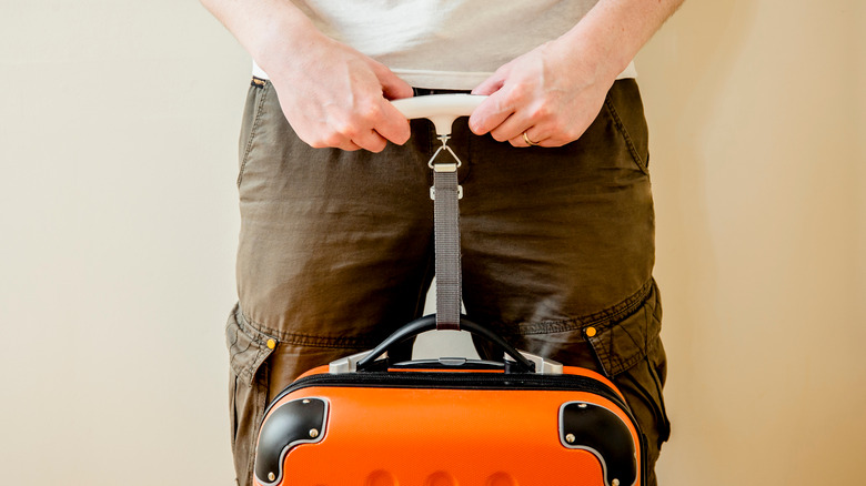 man weighing luggage with scale