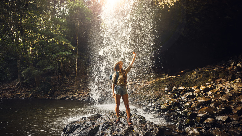 young woman standing under waterfall